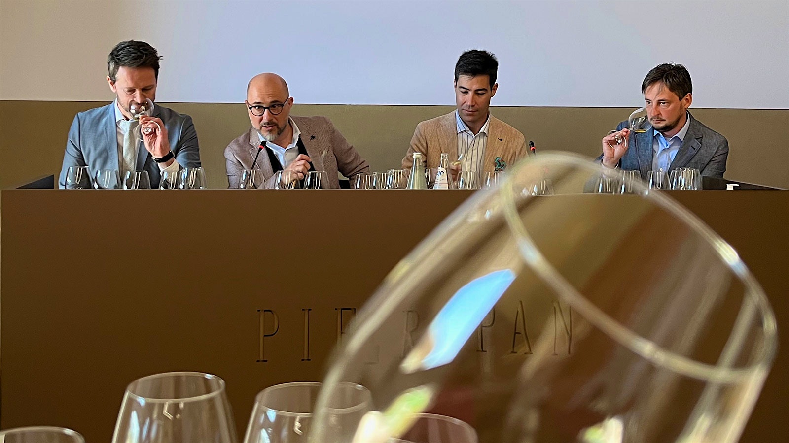 At the 50th anniversary Calvarino tasting, four men sit at a dias with Pieropan emblazoned on front. From left to right, they are Dario Pieropan, wine educators Filippo Bartolotta and Gabriele Gorelli, and Andrea Pieropan. Wine glasses fill the foreground